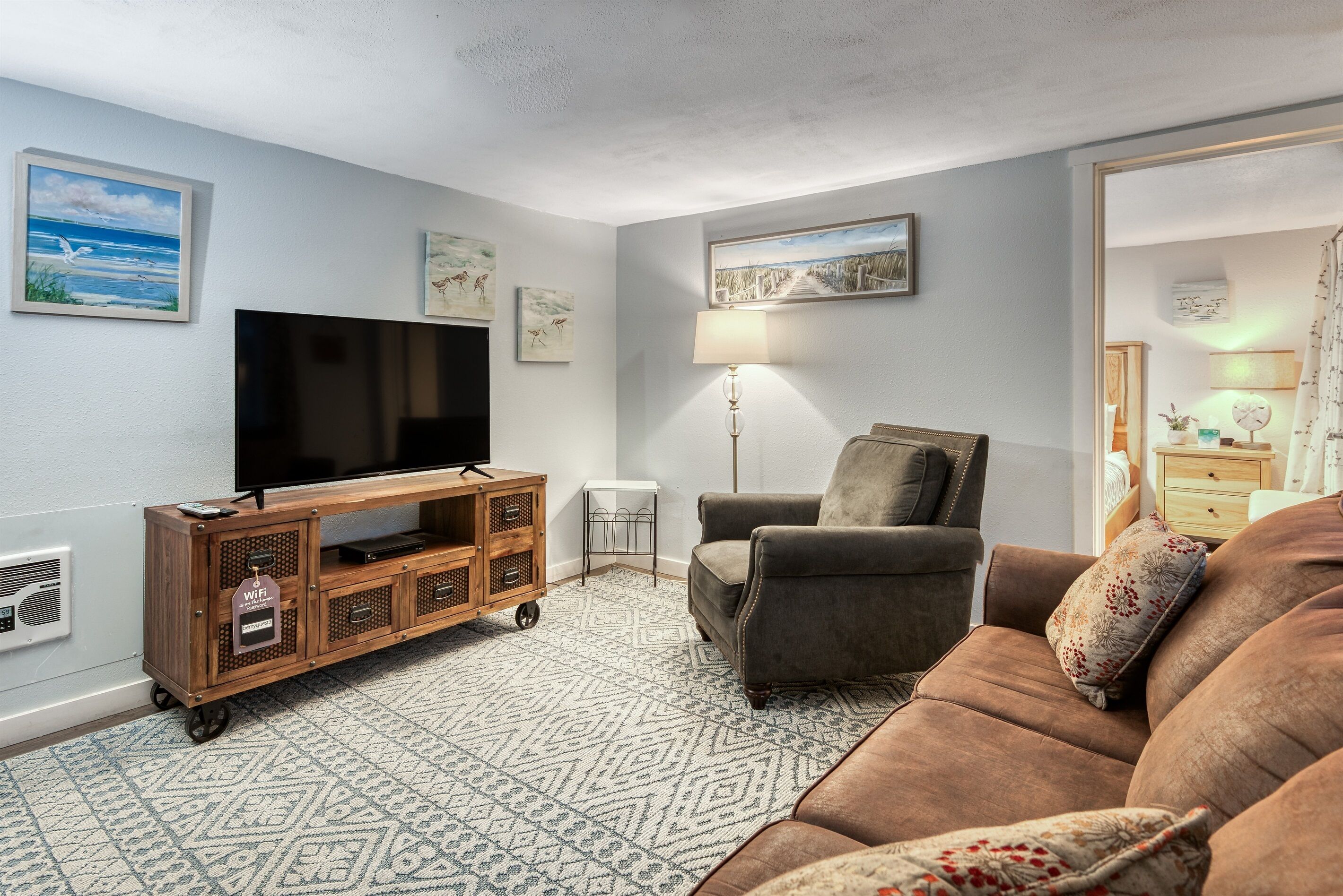 Ein Wohnzimmer mit Fernseher auf einer Holzkommode, einer Couch, einer Lampe und einem gemusterten Teppich.