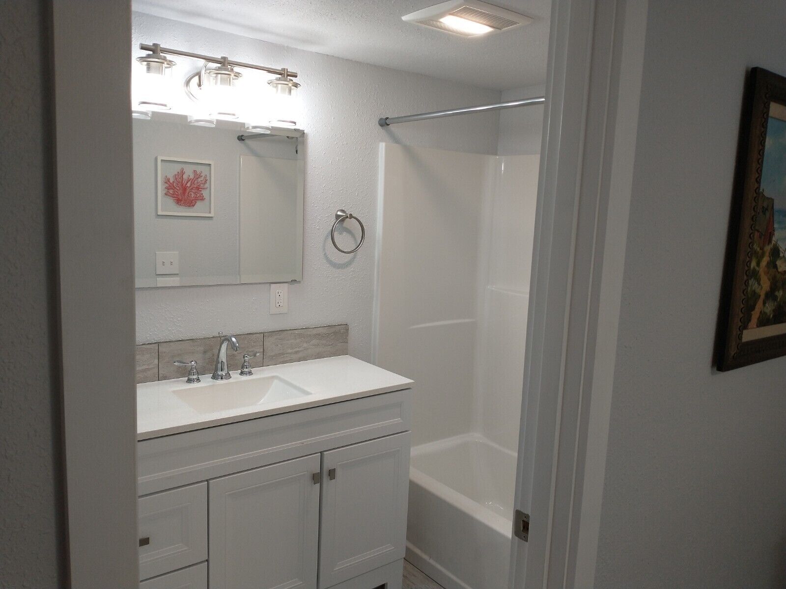 A bathroom with a white vanity, a mirror, a towel ring, and a shower enclosure.