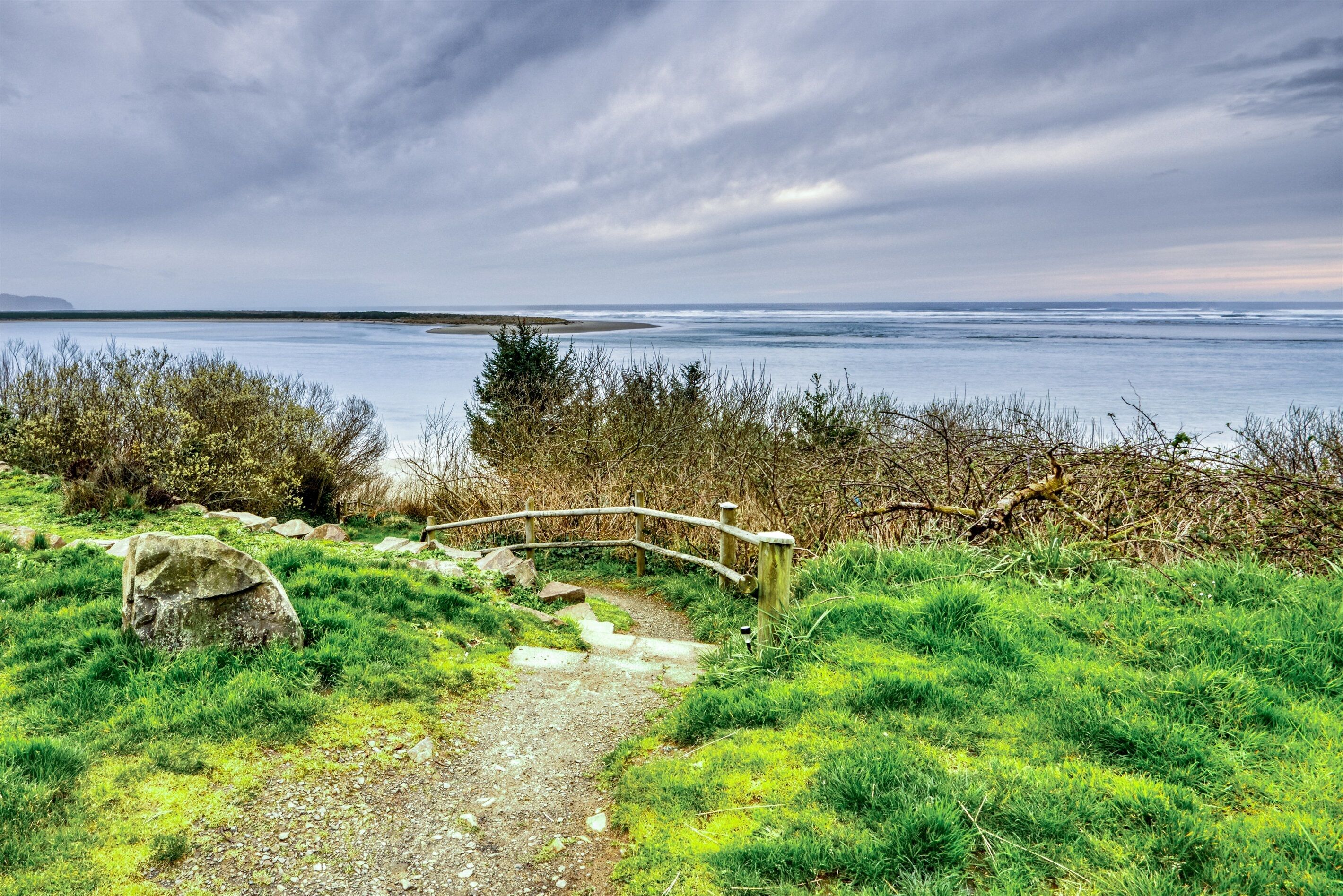 A coastal path with a wooden bridge leading to a grassy area and the sea.
