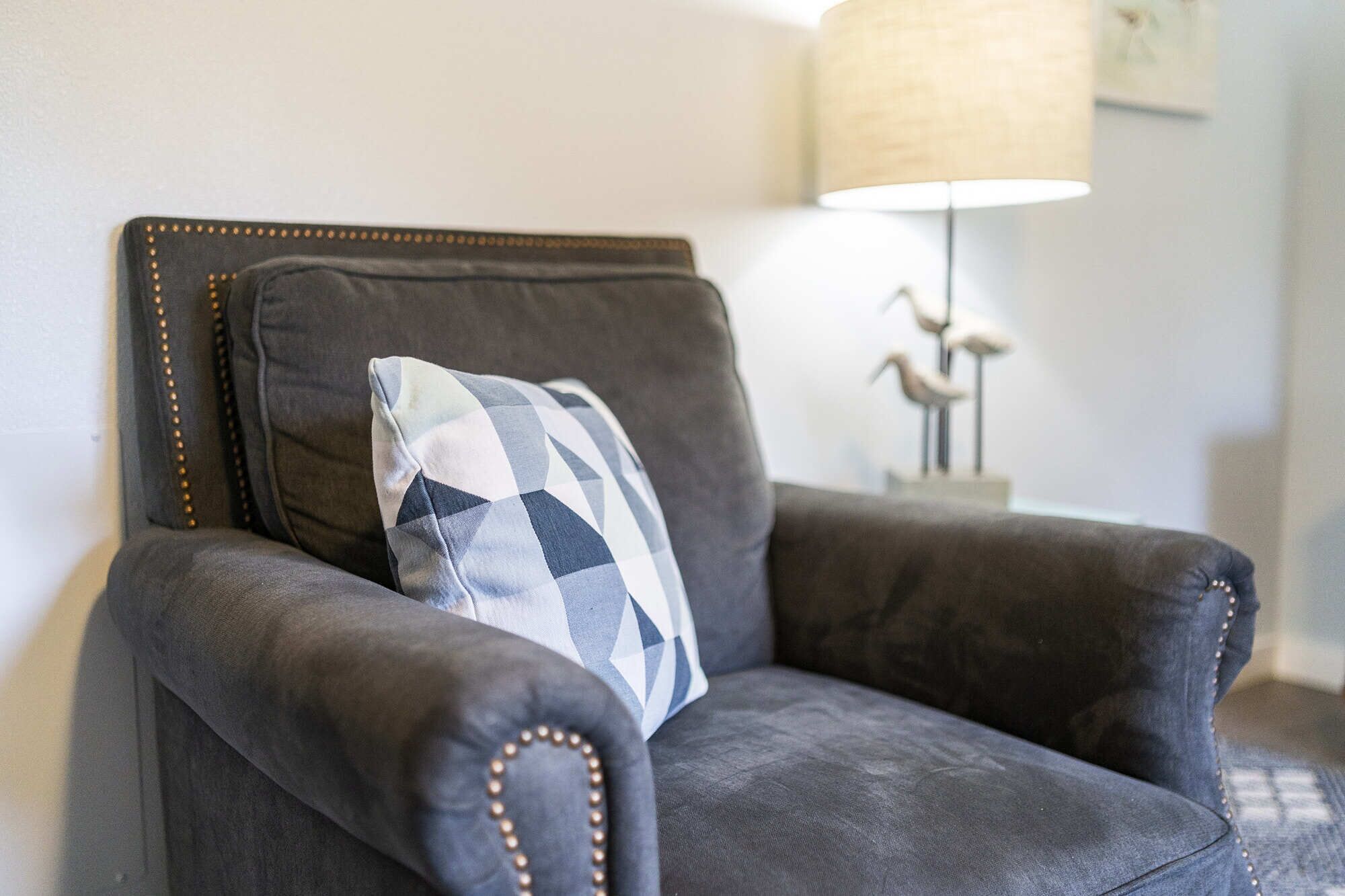A dark leather armchair with a checkered pillow and a lamp in the background.