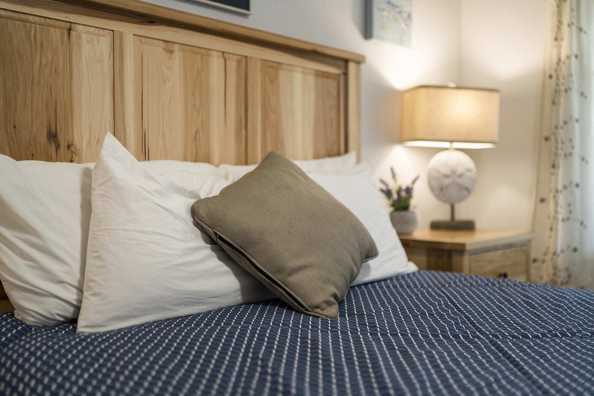 Un lit bien fait, avec une tête de lit en bois, des oreillers blancs et beiges, et une couvre-lit à rayures bleues.