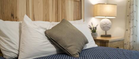 Un lit bien fait, avec une tête de lit en bois, des oreillers blancs et beiges, et une couvre-lit à rayures bleues.