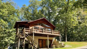 A wooden cabin with a balcony and a staircase leading to the entrance. - Pet friendly, hot tub, close to Hocking Hills! (McArthur)