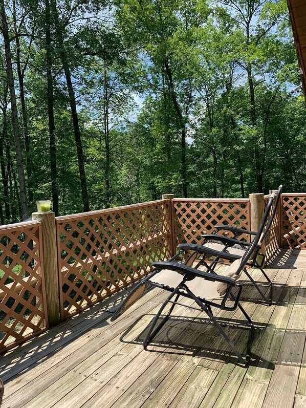 A wooden deck with a lattice railing, two lounge chairs, and a view of a forested area. - Pet friendly, hot tub, close to Hocking Hills! (McArthur)
