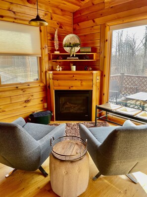 Cozy log-furnished room with a fireplace, armchairs, and a round table, offering a view of the outdoors.