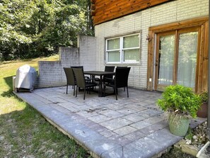 An outdoor patio with a table and chairs, a covered grill, and a potted plant.