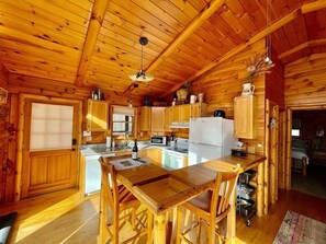 A wooden cabin kitchen with a central island, wooden cabinets, and a refrigerator. - Pet friendly, hot tub, close to Hocking Hills! (McArthur)