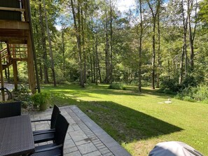 A patio with a table and chairs, surrounded by a grassy area and trees.