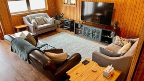A cozy living room with a leather sofa, a grey couch, and a wooden coffee table. A flat-screen TV is mounted on the wall, and there is a small wooden side table. - Pet friendly, hot tub, close to Hocking Hills! (McArthur)