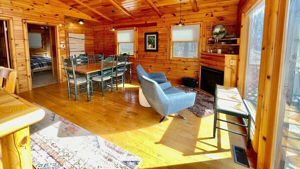 A wooden cabin interior with a dining area, a blue armchair, and a kitchen area. - Pet friendly, hot tub, close to Hocking Hills! (McArthur)