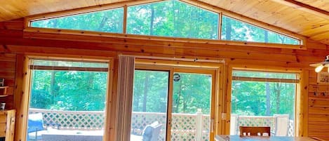 A wooden cabin interior with a dining area, large sliding glass doors, and a ceiling fan.