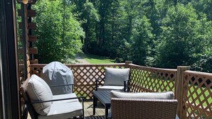 A wooden deck with outdoor furniture, including a wicker chair and a cushioned chair, and a wooden fence. - Pet friendly, hot tub, close to Hocking Hills! (McArthur)