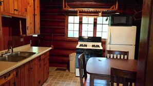 A wooden cabin interior with a kitchen area, including a stove, sink, and refrigerator. - Private Lake Superior Log Cabin on the Beach (Au Train)