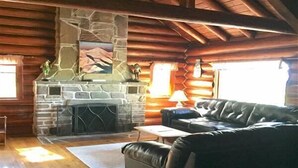 A log cabin interior with a stone fireplace, leather sofa, and wooden beams. - Private Lake Superior Log Cabin on the Beach (Au Train)
