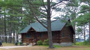 A log cabin with a porch and steps leading to the entrance, surrounded by trees. - Private Lake Superior Log Cabin on the Beach (Au Train)