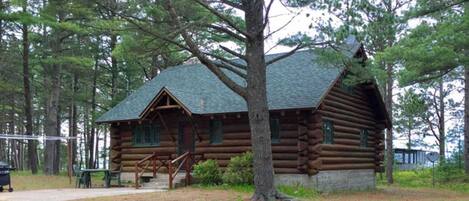 A log cabin with a porch and steps leading to the entrance, surrounded by trees.