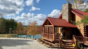 Una cabaña de troncos con chimenea de piedra, un porche de madera y vistas a un lago.