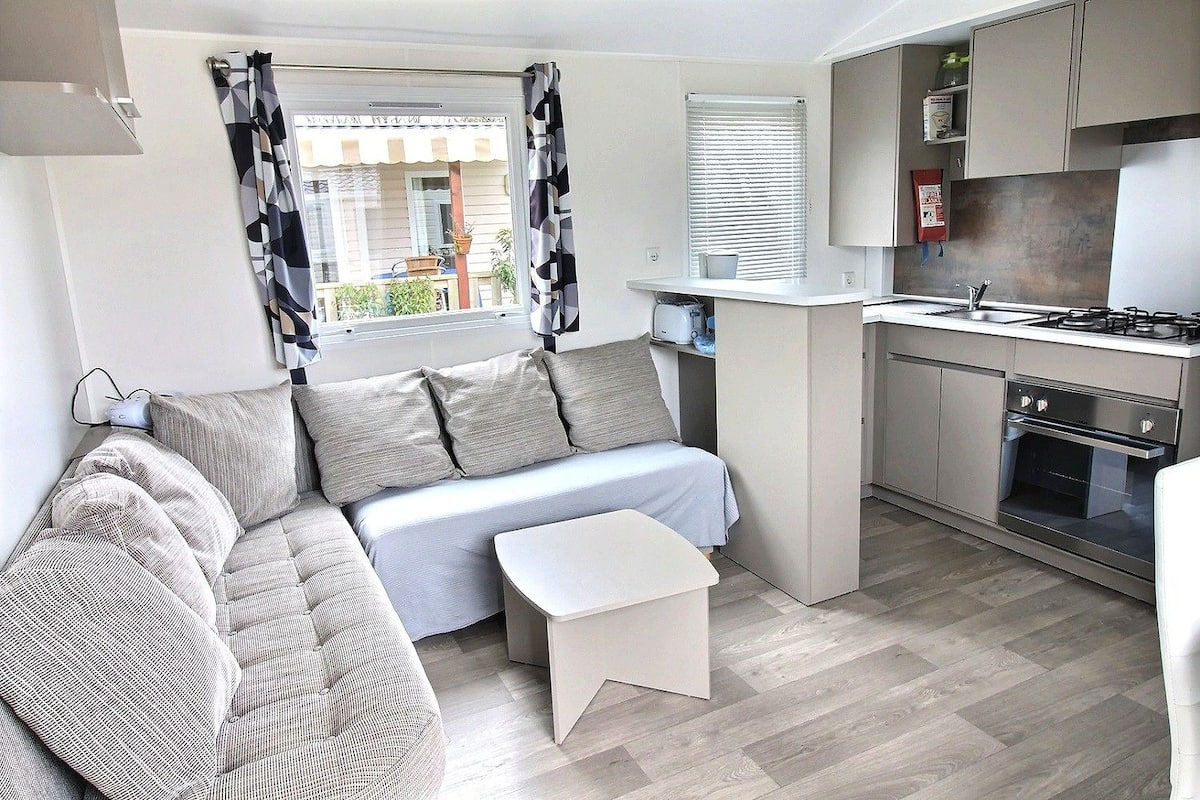 A compact living space with a sofa, a small table, a kitchenette, and a window with curtains.