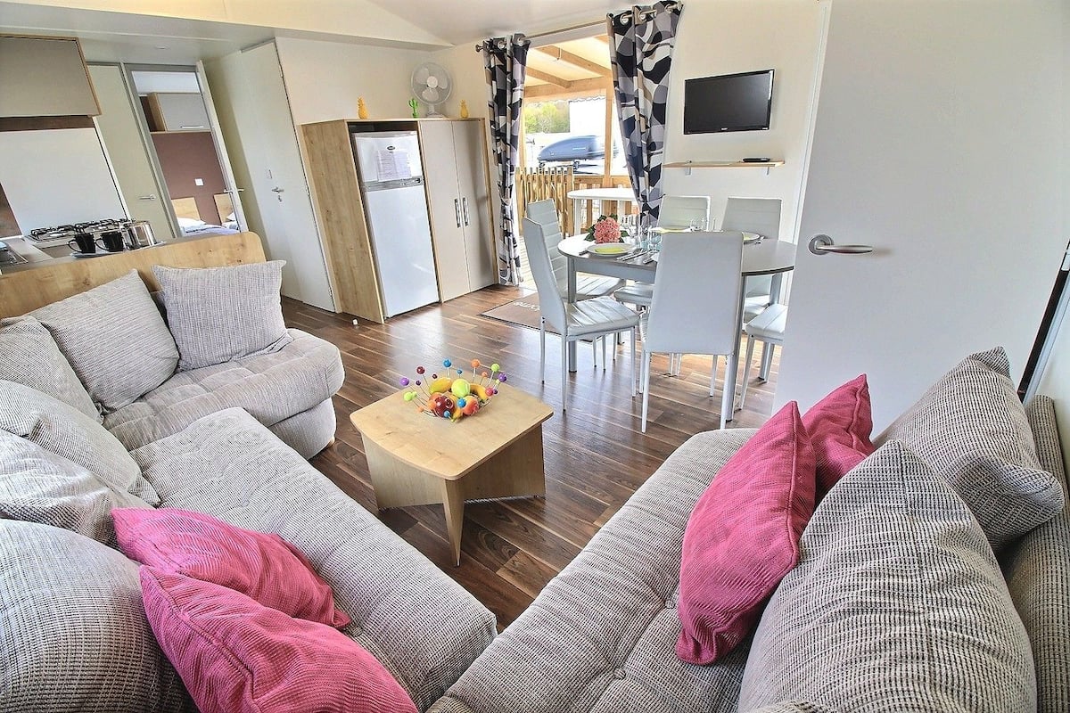 A modern living room with a sofa set, a wooden coffee table, and a dining area with a TV.