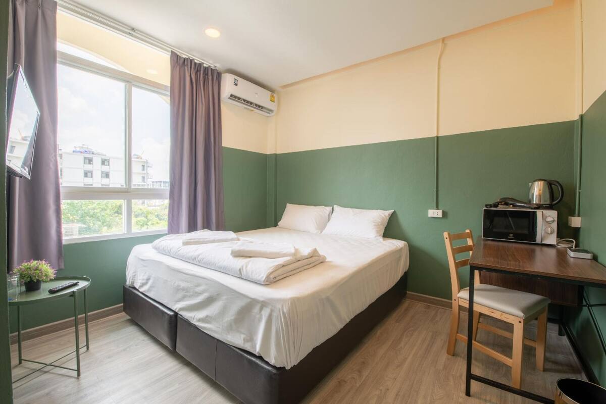 A bedroom with a bed, a desk, a chair, and an air conditioning unit.