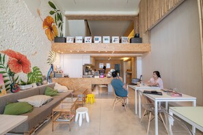 A modern interior with a sofa, coffee table, and a dining area. There is a counter with a person working behind it. - Spacy BKK (Bangkok)
