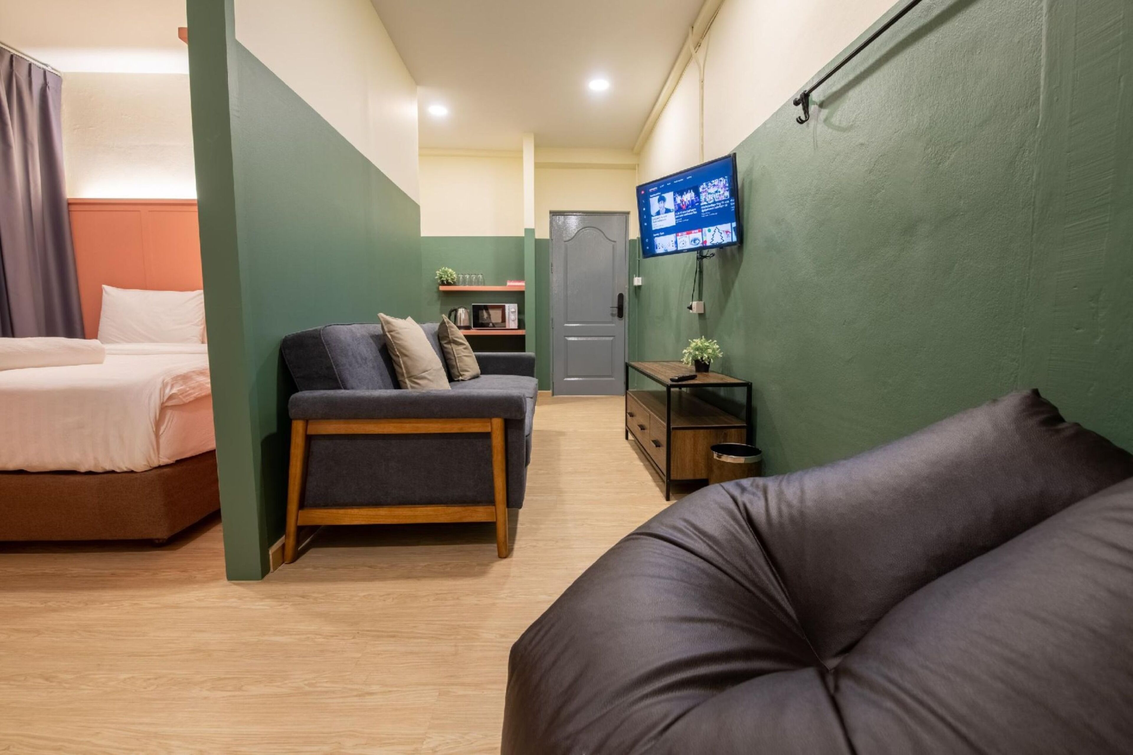 A compact hotel room with a bed, a sofa, a TV, and a small table with a plant.