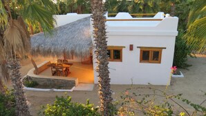 A white building with a thatched roof patio, surrounded by palm trees and greenery. - Villa Gardenia - Casa Jazmín directly on the sea (Todos Santos)
