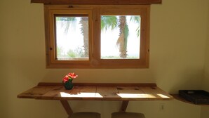 A wooden bench with a small table and two chairs underneath a window with a view of palm trees. - Villa Gardenia - Casa Jazmín directly on the sea (Todos Santos)