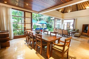 Relax in a spacious room with a high ceiling, dining area, and comfortable seating, offering views of lush greenery.