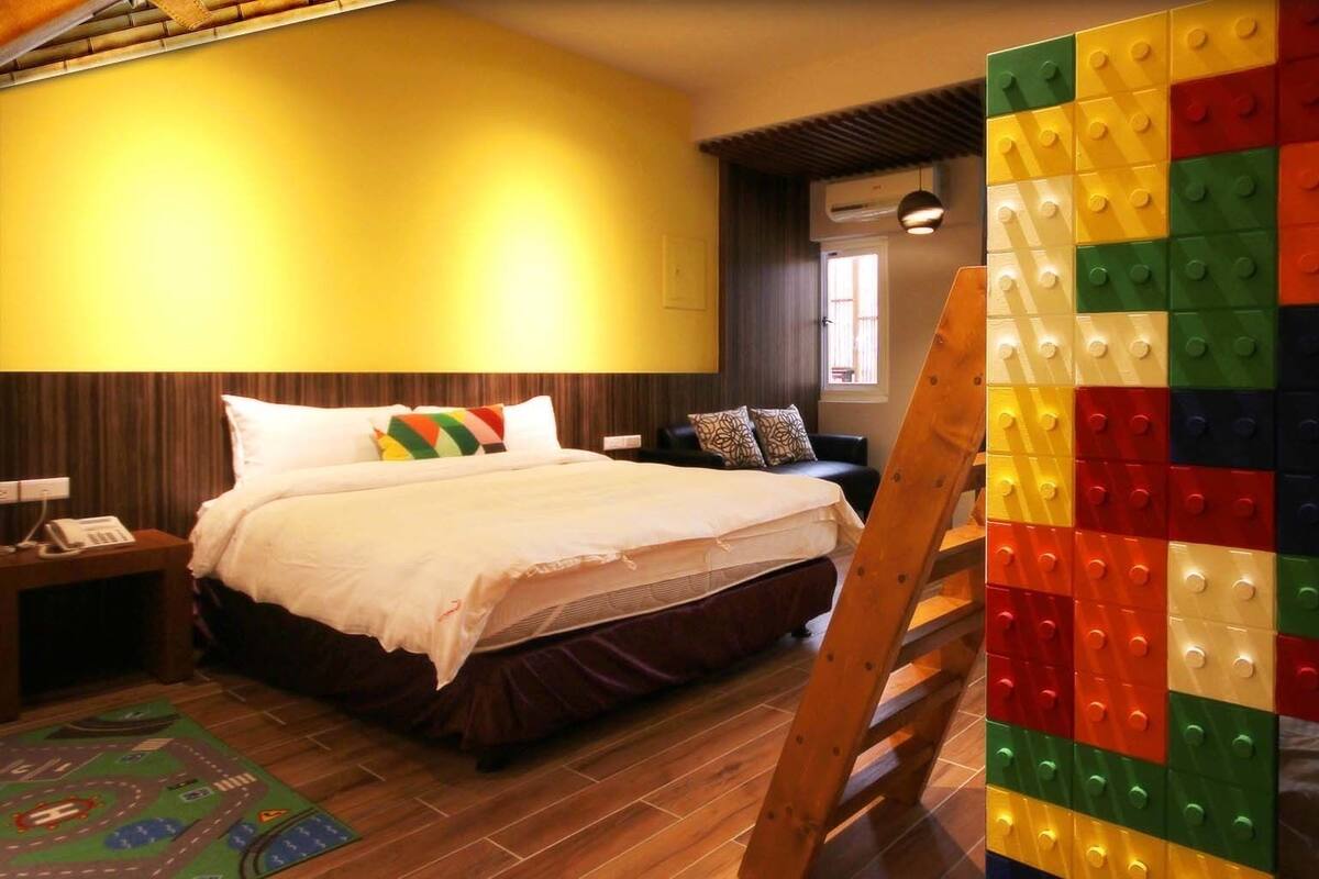 A hotel room with a bed, a nightstand, a wooden floor, and a colorful wall decoration.