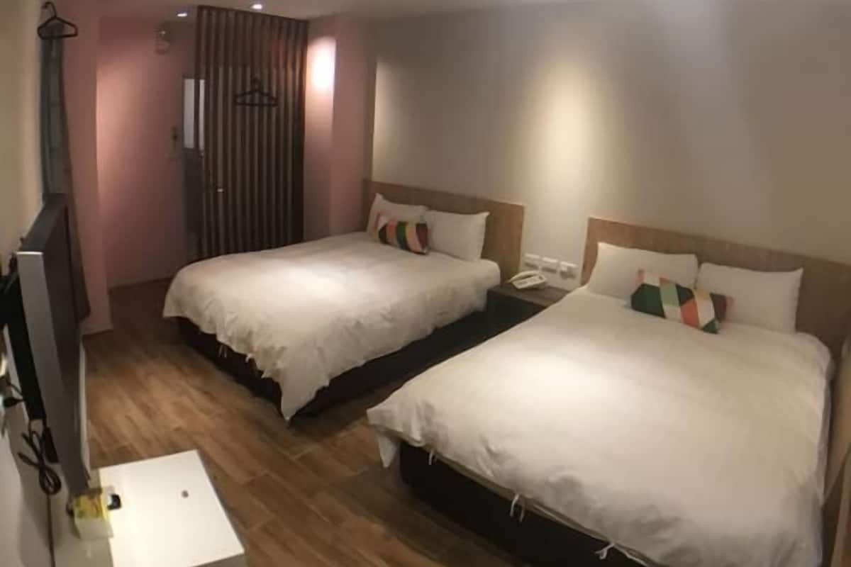 A hotel room with two beds, a small desk, a TV, and a mirror.