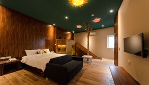 A modern bedroom with a wooden floor, a bed with colorful pillows, a black sofa, a TV, and a staircase. - Rainbow House (Yuchi)