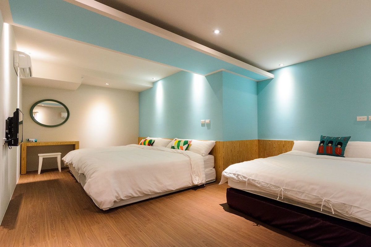 A hotel room with two beds, a wooden headboard, a small desk, and a mirror on the wall.