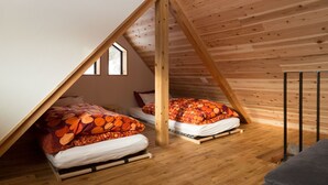 A loft bedroom with two beds, wooden beams, and a sloped ceiling. - Harvest Eco House (Nozawaonsen)