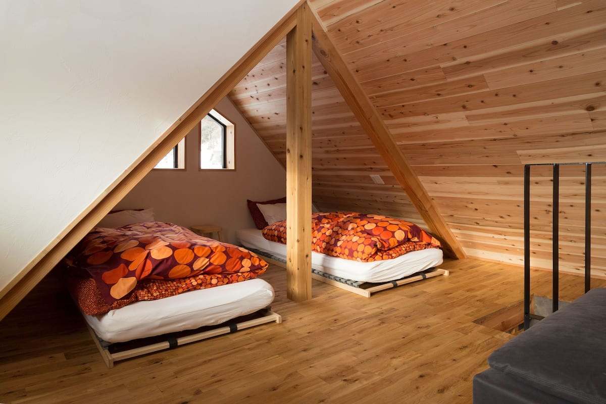 Une chambre à coucher de style « loft », avec deux lits, des poutres en bois et un plafond en pente.