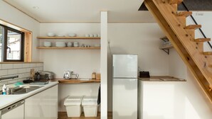 A modern kitchen with white cabinets, wooden shelves, a stainless steel sink, and a built-in refrigerator. - Harvest Eco House (Nozawaonsen)