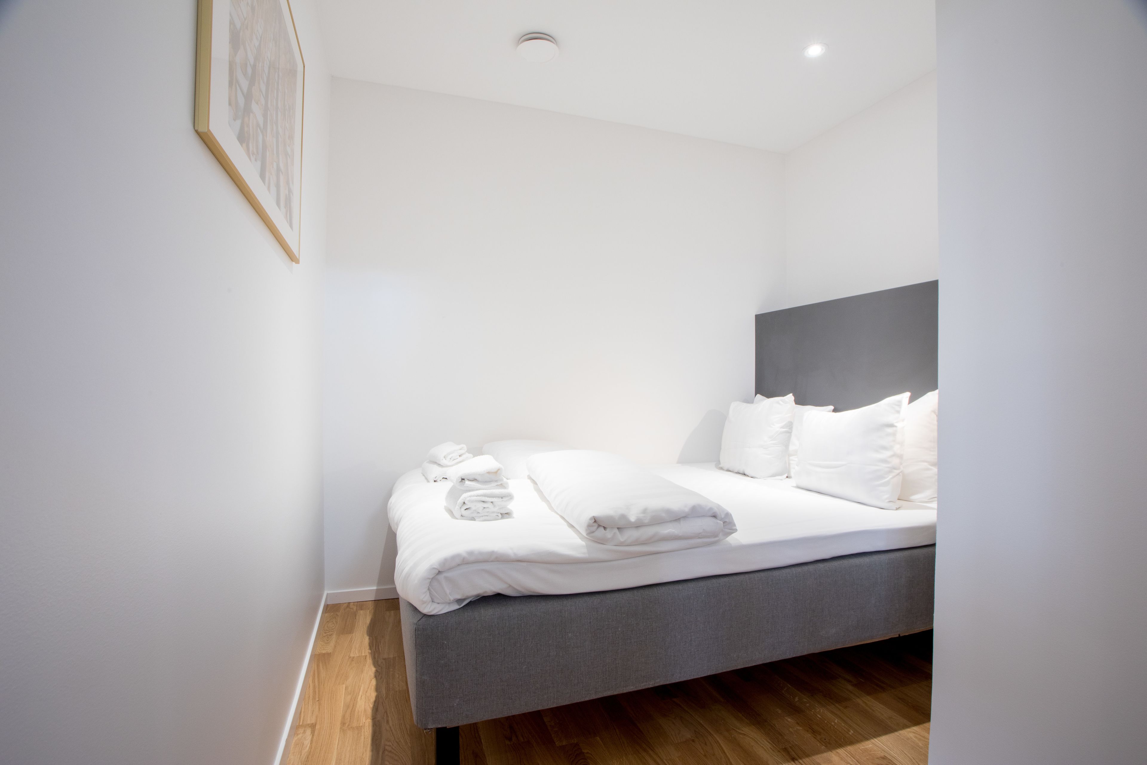 A modern hotel room with a grey bed, white linens, and a framed picture on the wall.