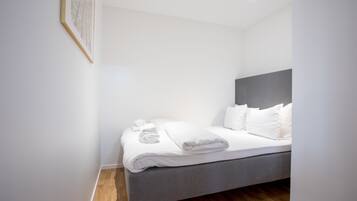 A modern hotel room with a grey bed, white linens, and a framed picture on the wall.