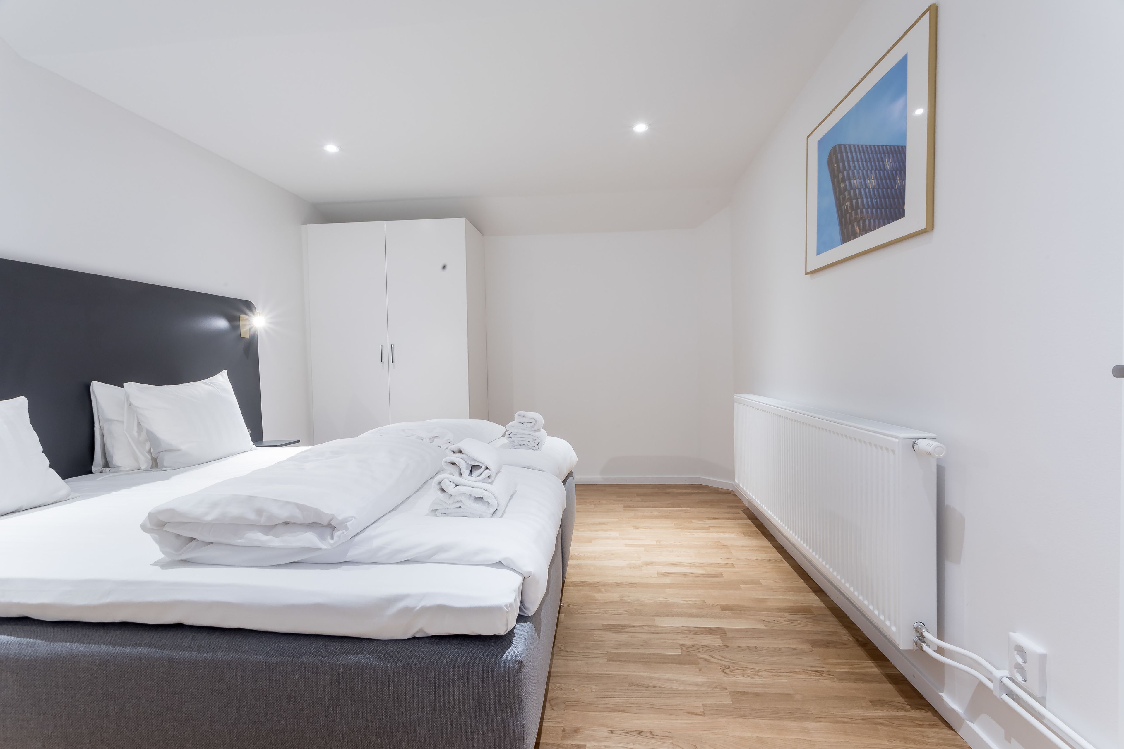 A modern hotel room with a neatly made bed, a large wardrobe, and a framed picture on the wall.