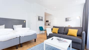 A modern hotel room with a bed, a sofa, a coffee table, and a view of the kitchen area.