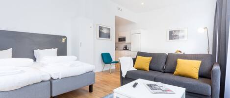 Ein modernes Hotelzimmer mit Bett, Sofa, Couchtisch und Blick auf den Küchenbereich.