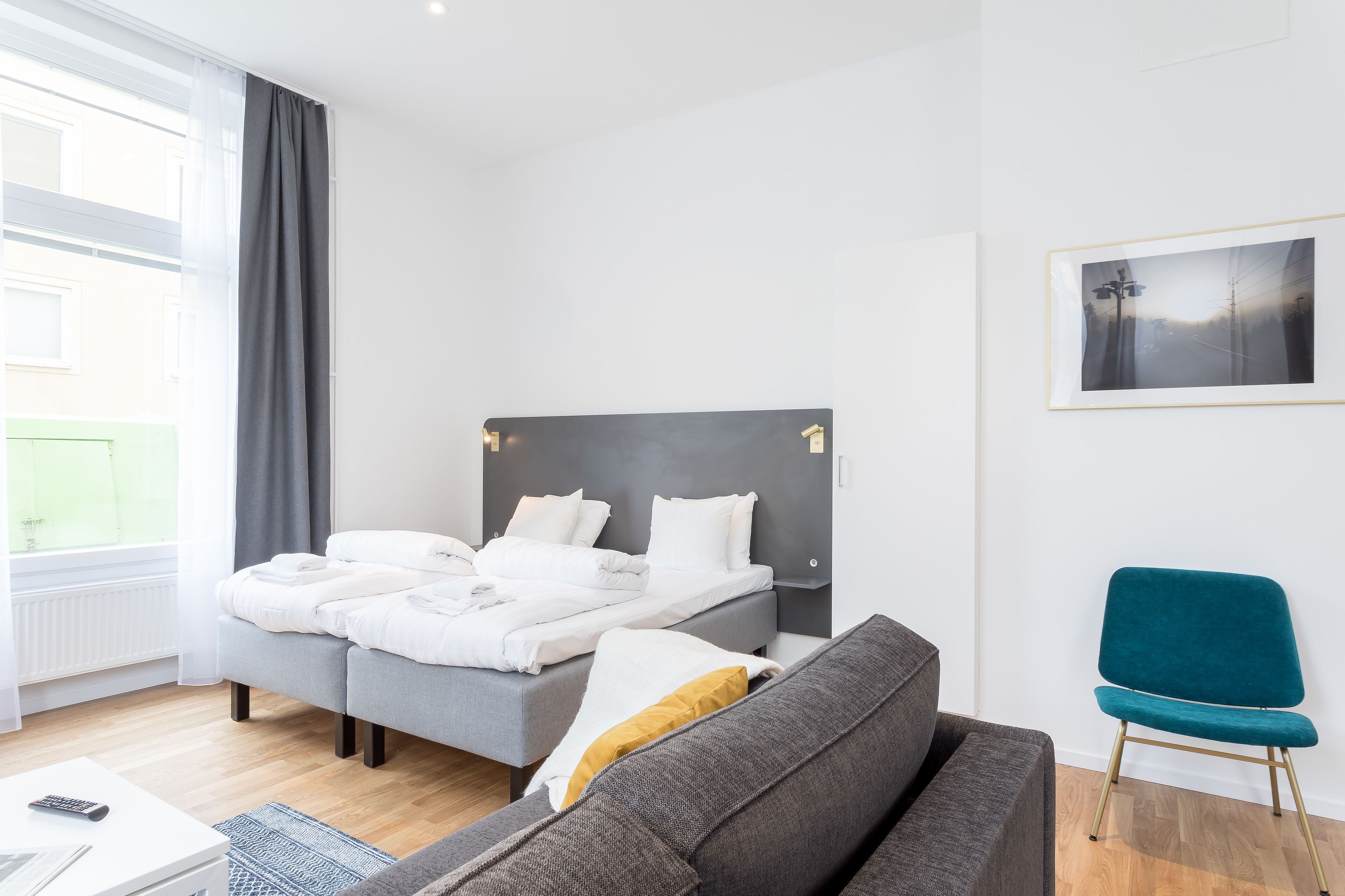 A modern hotel room with a bed, a sofa, a chair, and a framed picture on the wall.