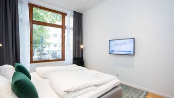 A modern hotel room with a large bed, a television mounted on the wall, and a window with curtains.
