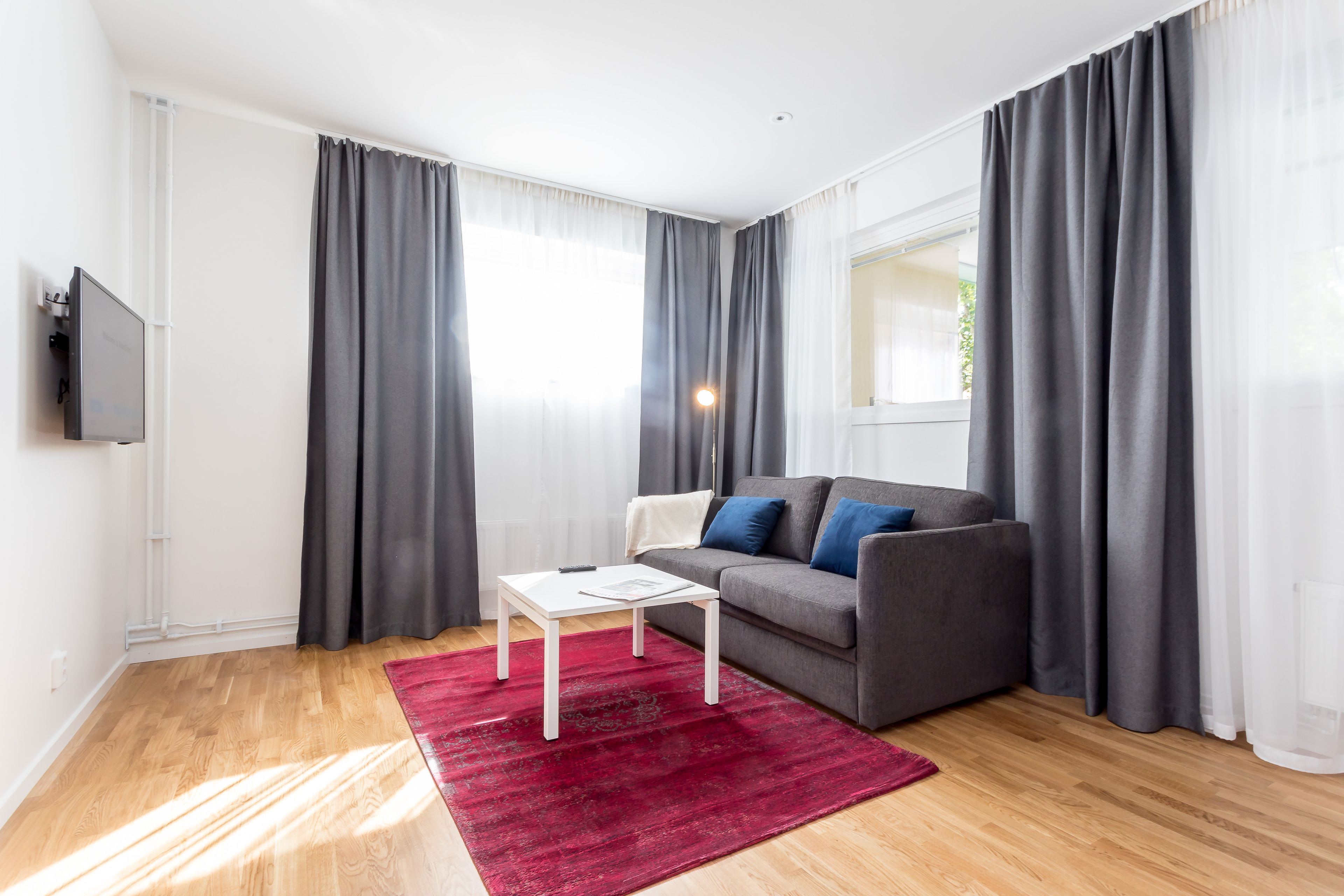 Un salon moderne avec un canapé gris, une table basse blanche et un tapis rouge.