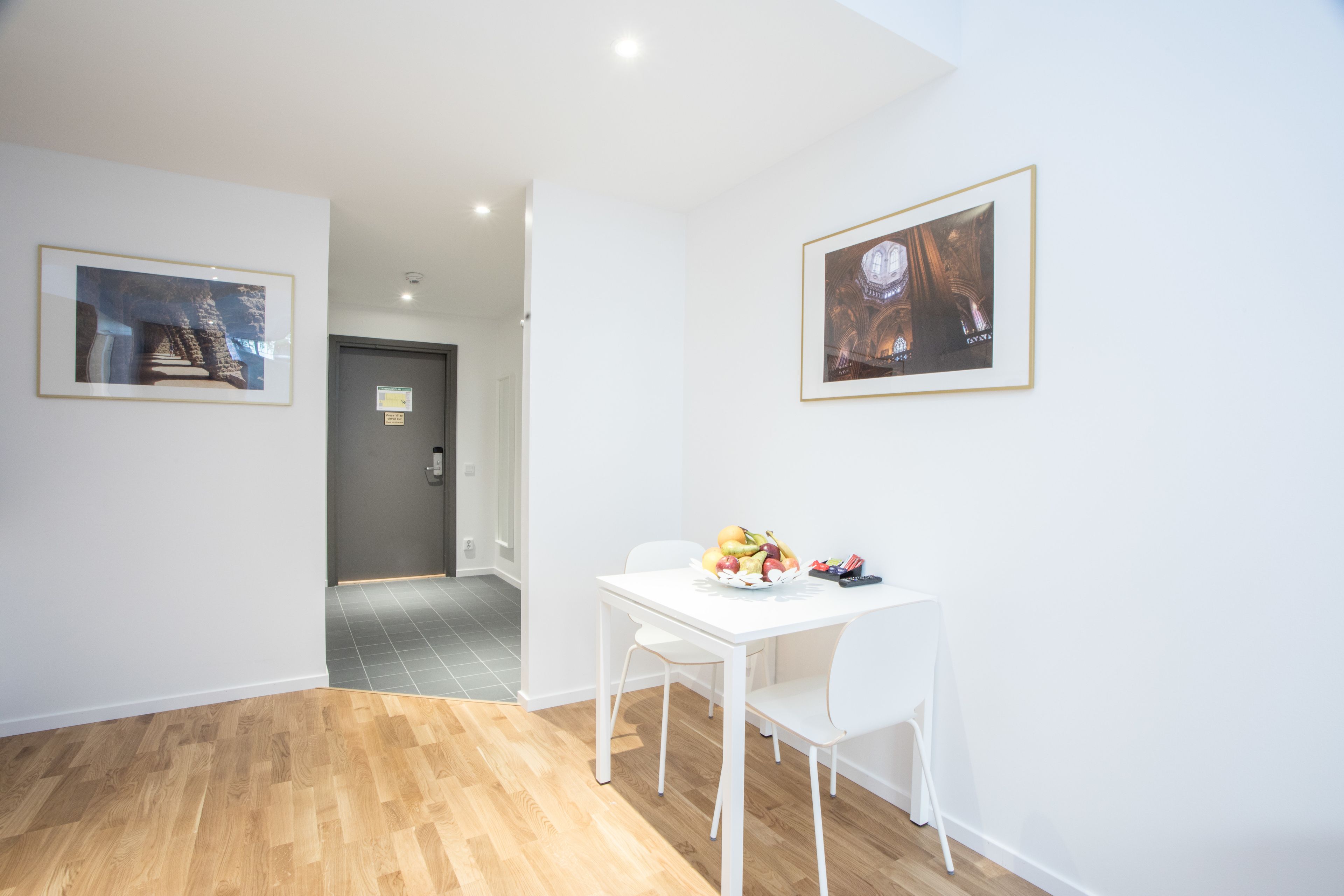 A modern room with a white table set with fruit, two framed pictures on the wall, and a wooden floor.