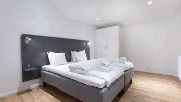A modern bedroom with a grey bed, white bedding, a black headboard, and a wooden floor.