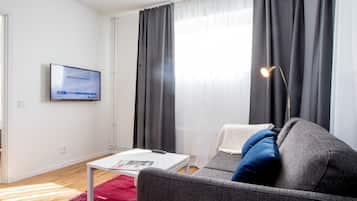 A modern living room with a grey sofa, a white coffee table, and a flat-screen TV mounted on the wall.