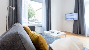 Een moderne woonkamer met een grijze bank, een geel kussen, een witte salontafel en een televisie waarop een welkomstbericht staat.