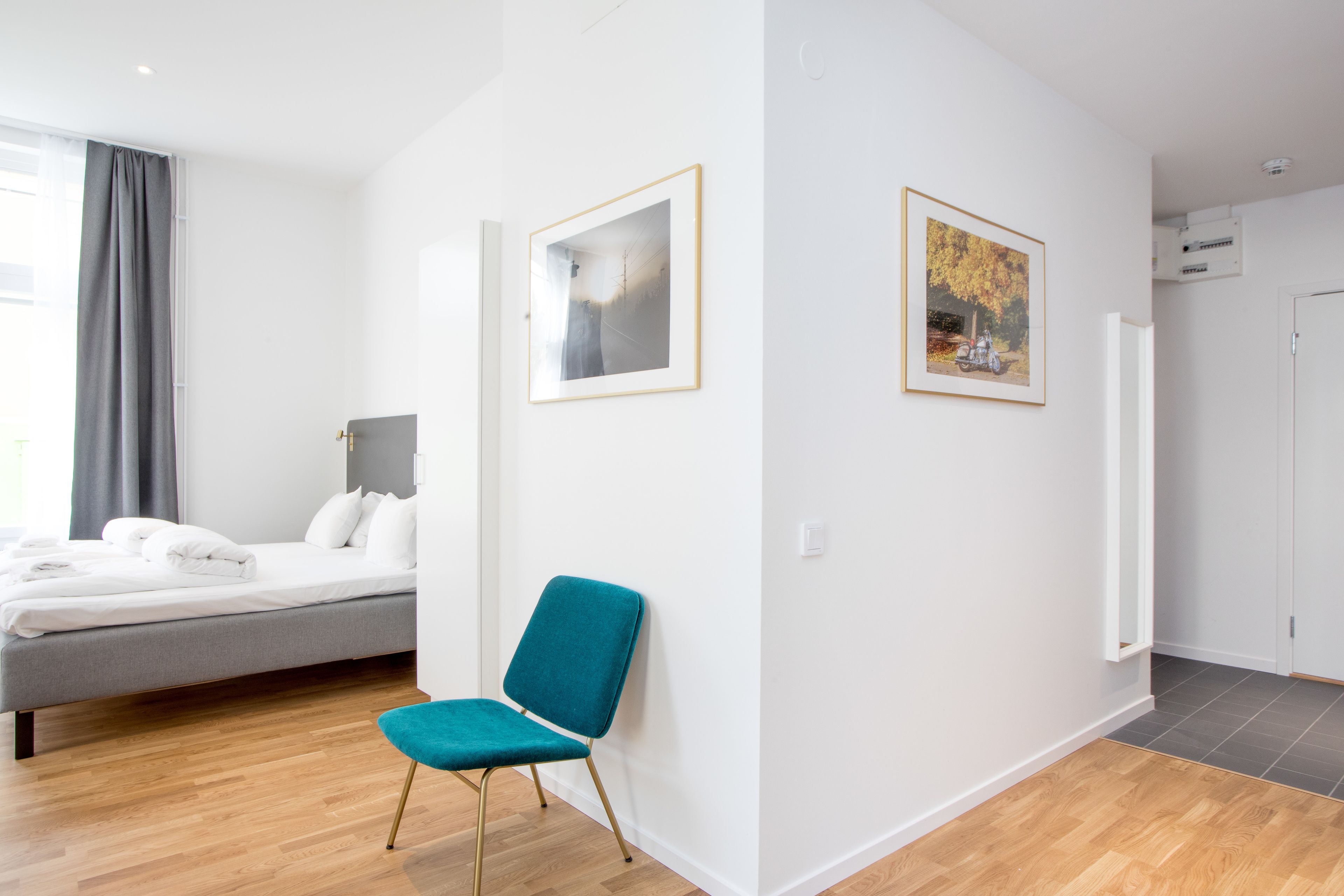 A modern hotel room with a bed, a teal chair, two framed pictures, and a shower area.