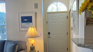 Uma sala de estar com sofá, luminária, quadro emoldurado e porta que dá para outro cômodo.
